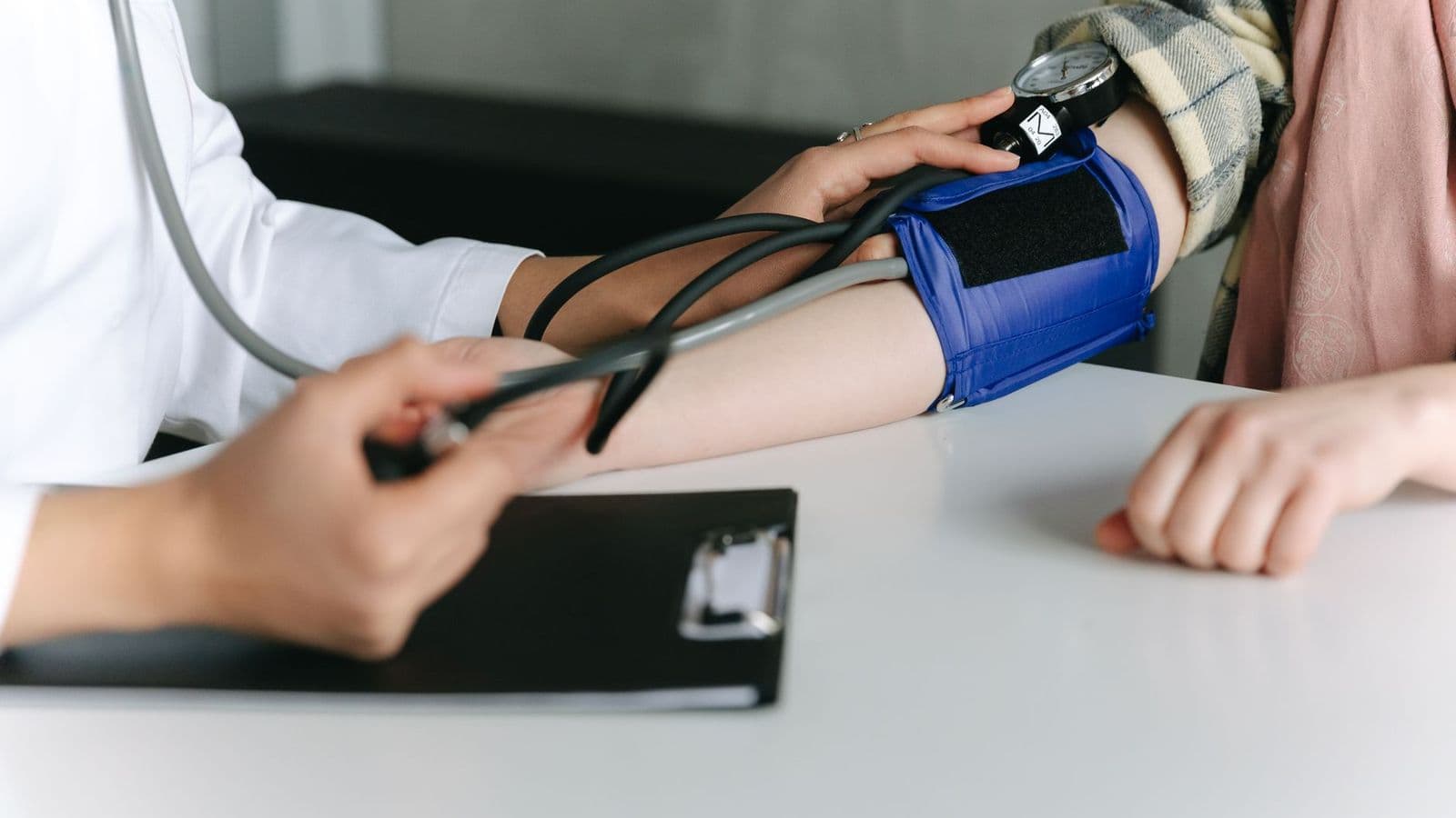 A clinician wrapping a blood pressure cuff around a patient's upper arm.