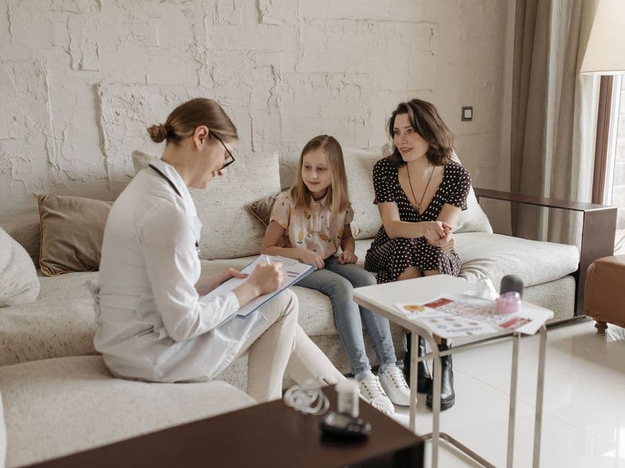 A health worker visiting a family at home, sitting with them in their living room.