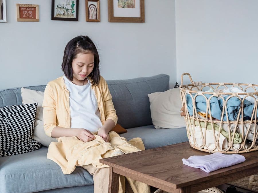 A woman folding clean laundry into neat piles beside a laundry basket.