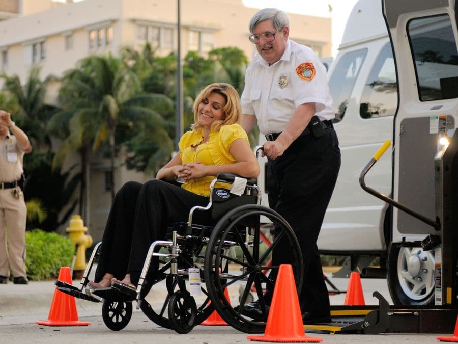 A wheelchair user being helped onto the powered lift of an accessible van.