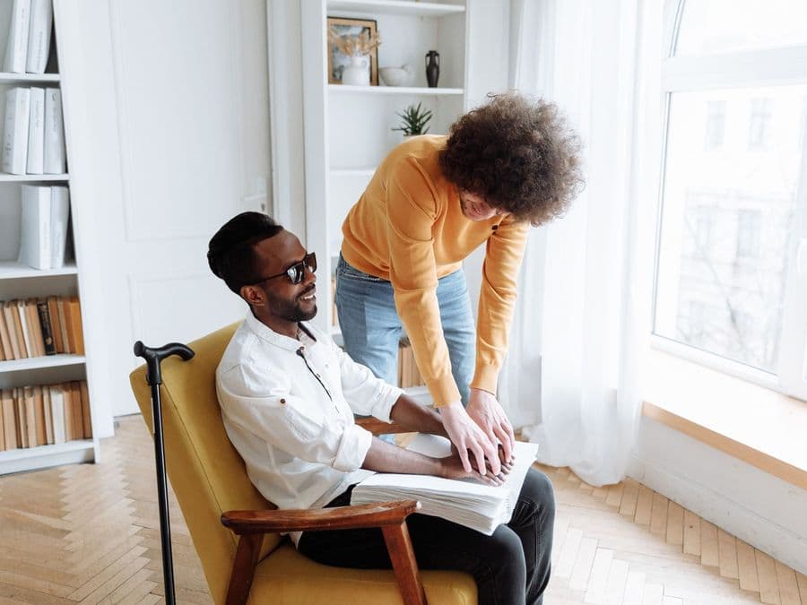 A support worker helping a man who is seated at home, going through something with him.