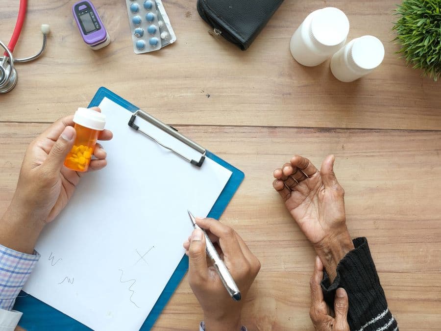 A hand holding a prescription bottle beside a clipboard of notes.