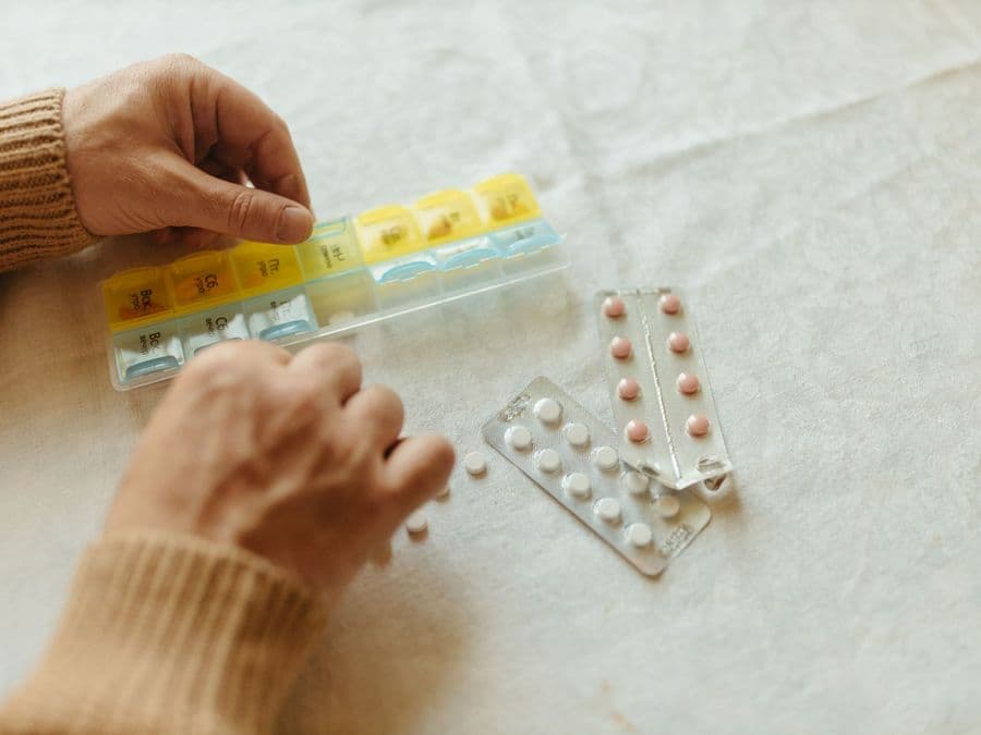 Hands sorting tablets into the compartments of a weekly pill organiser.