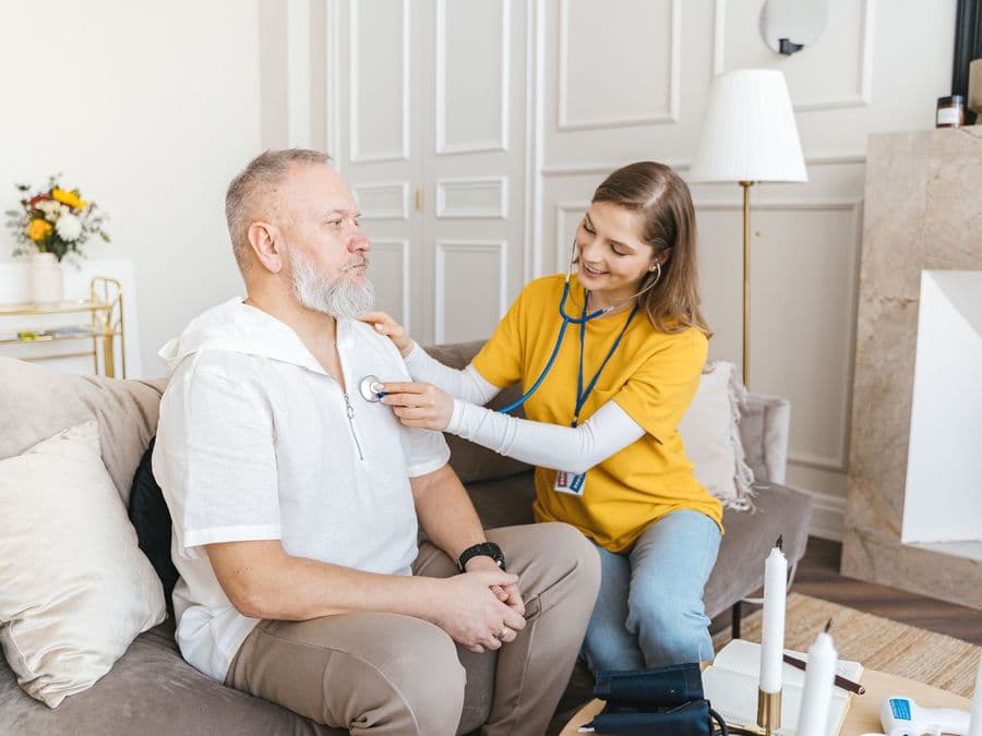 A trained care worker checking on an older man at home and noting down what she finds.
