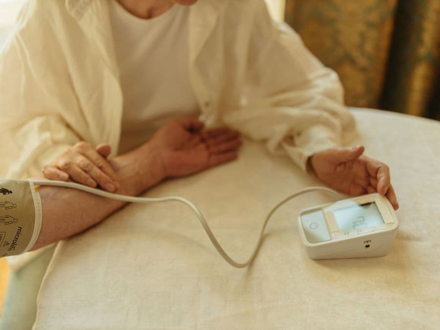 An older person using a blood pressure monitor at their own table at home.