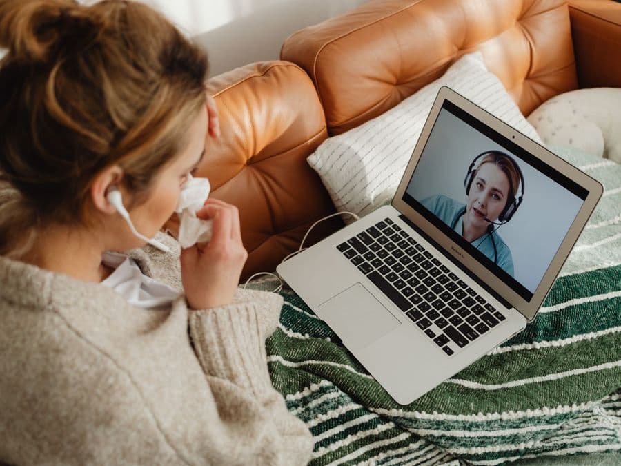 A woman at home on a video call with a clinician on her laptop screen.
