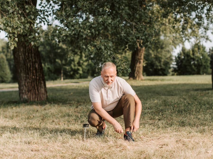 An older man stretching outdoors in a park before exercise.