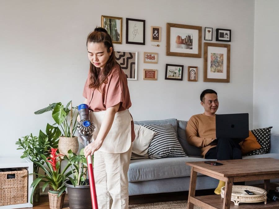 A care worker cleaning a living room while the resident sits comfortably nearby.