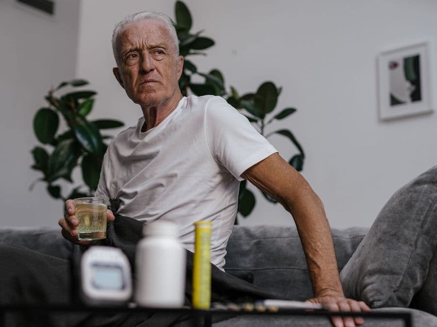 An older man at home reaching for his medication on the side table.